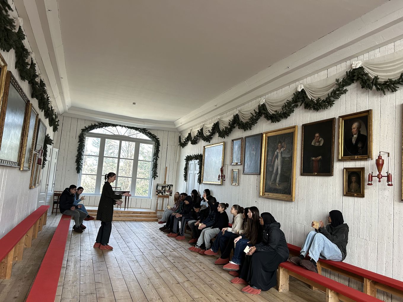 En person som snakker til en gruppe mennesker i et rom med kunst på veggene